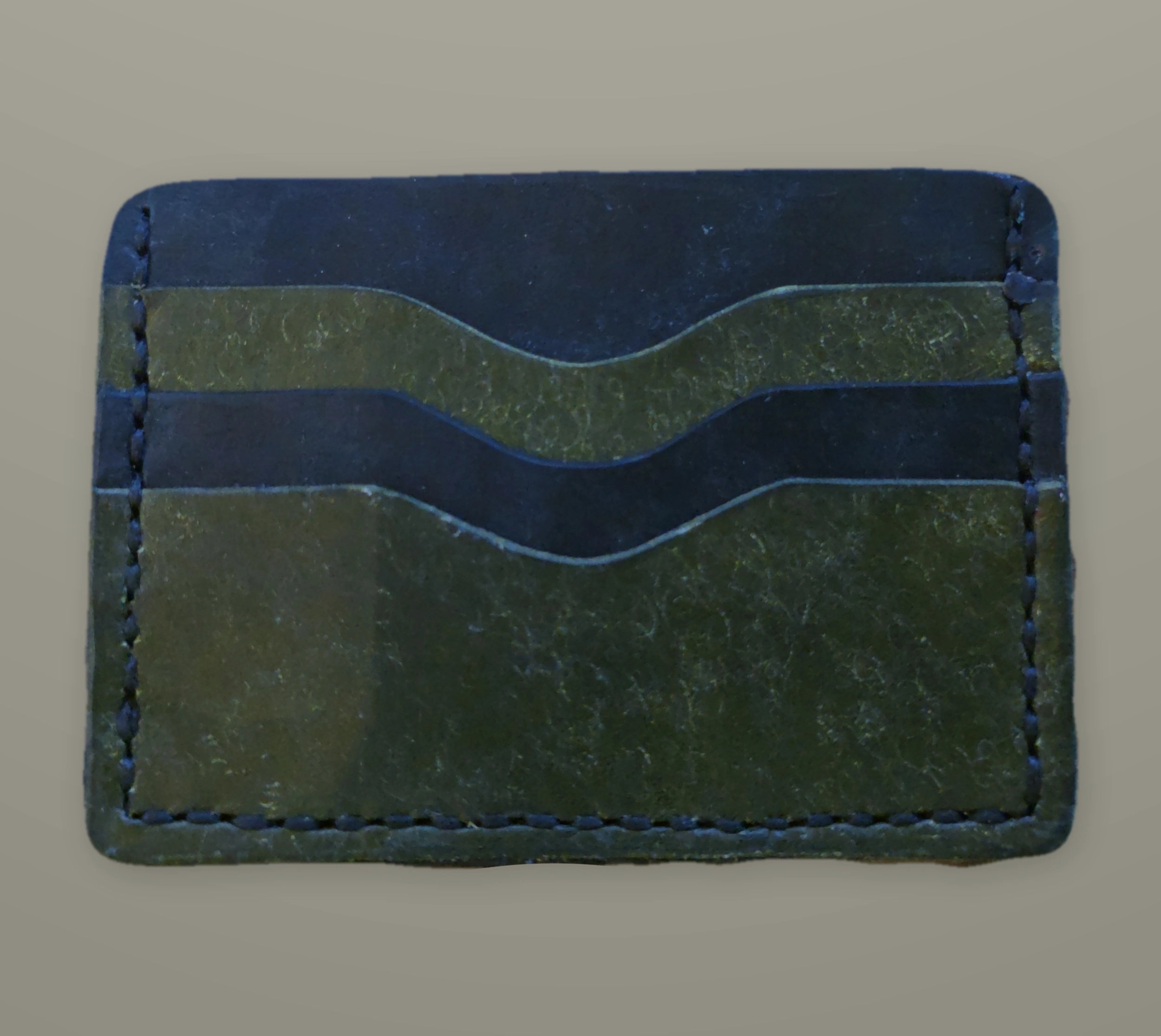 Black and olive handmade minimalist card wallet with two curved pockets on a muted slate background